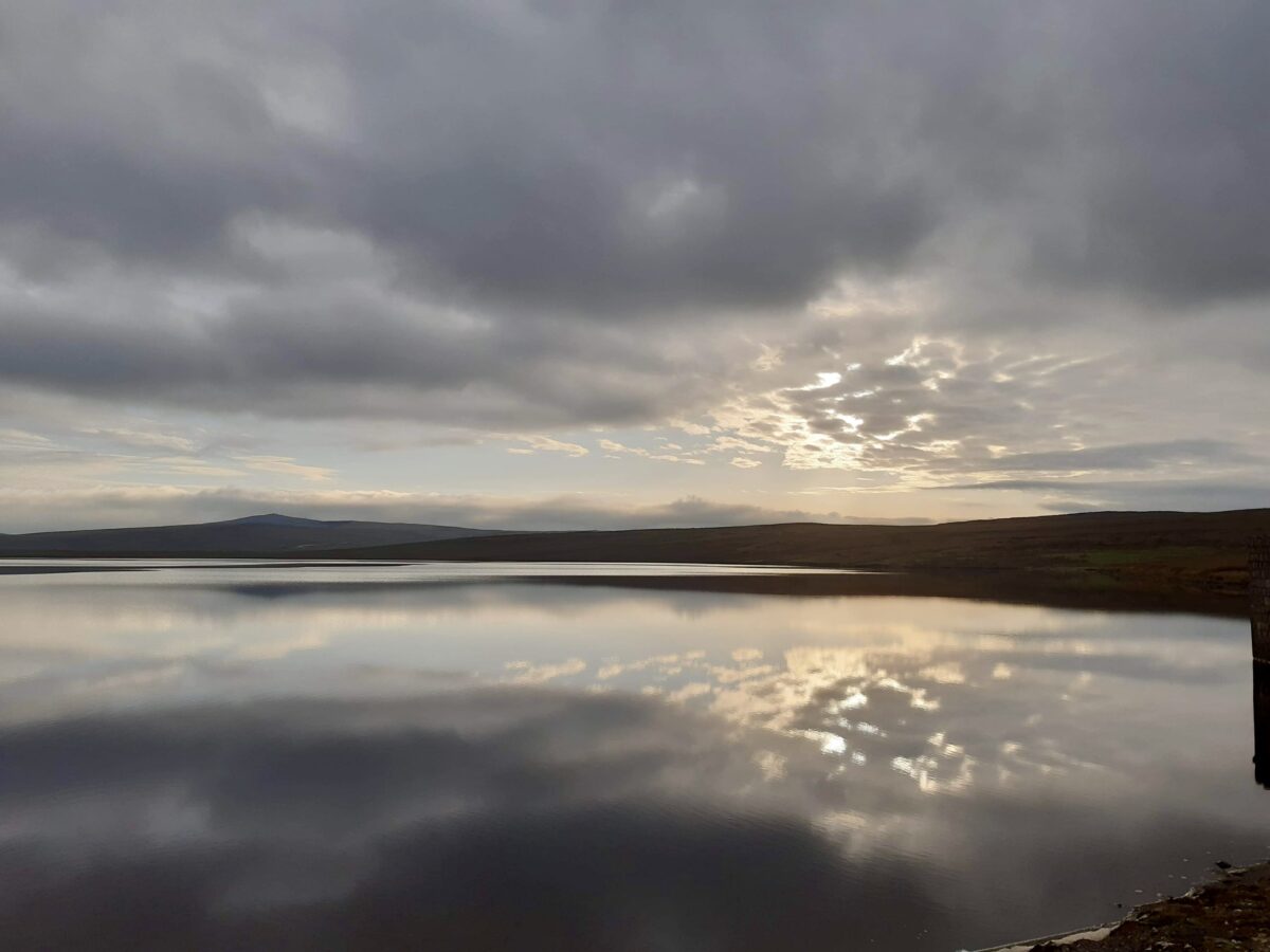 Sun rays peeking from behind a cloud and reflecting on the water of a big lake.