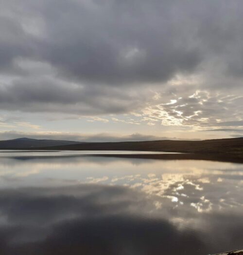 Sun rays peeking from behind a cloud and reflecting on the water of a big lake.