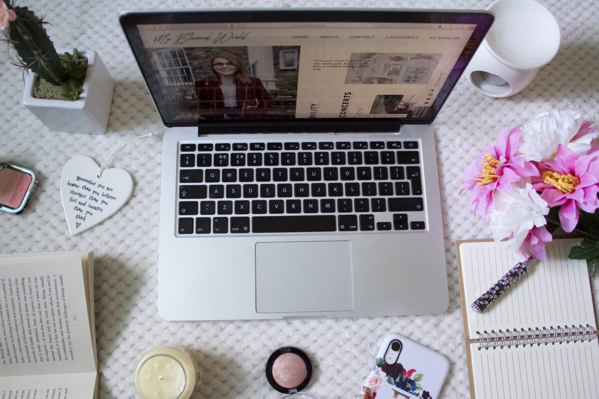 My Blurred World's homepage showing on a laptop screen which is surrounded by items such as fake flowers, a candle and a tealight holder