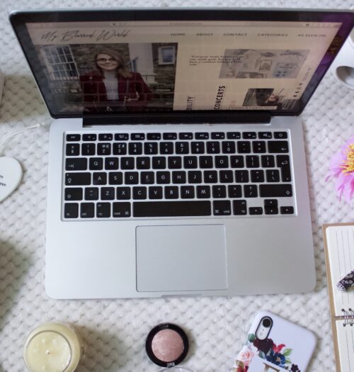 My Blurred World's homepage showing on a laptop screen which is surrounded by items such as fake flowers, a candle and a tealight holder