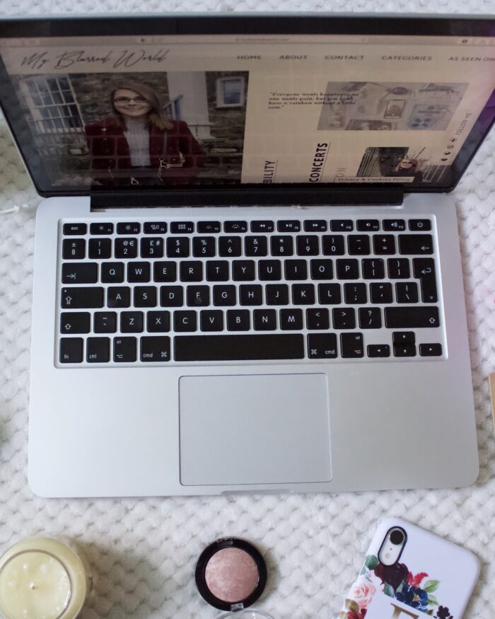 My Blurred World's homepage showing on a laptop screen which is surrounded by items such as fake flowers, a candle and a tealight holder