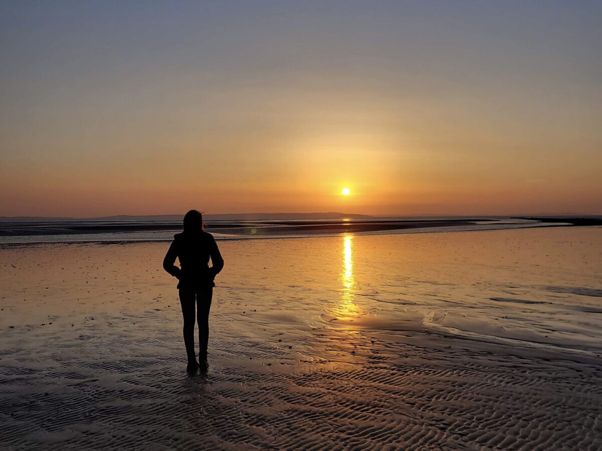 Elin looking out at the sun which sets over the sea. Her profile is cast in silhouette