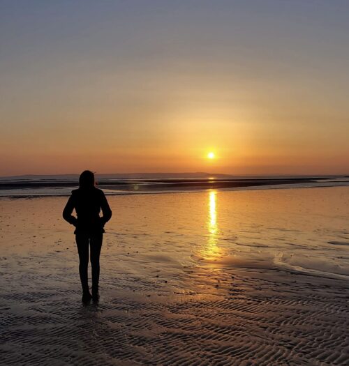 Elin looking out at the sun which sets over the sea. Her profile is cast in silhouette