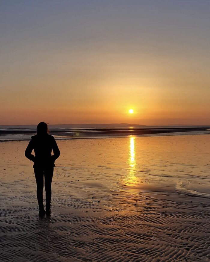 Elin looking out at the sun which sets over the sea. Her profile is cast in silhouette