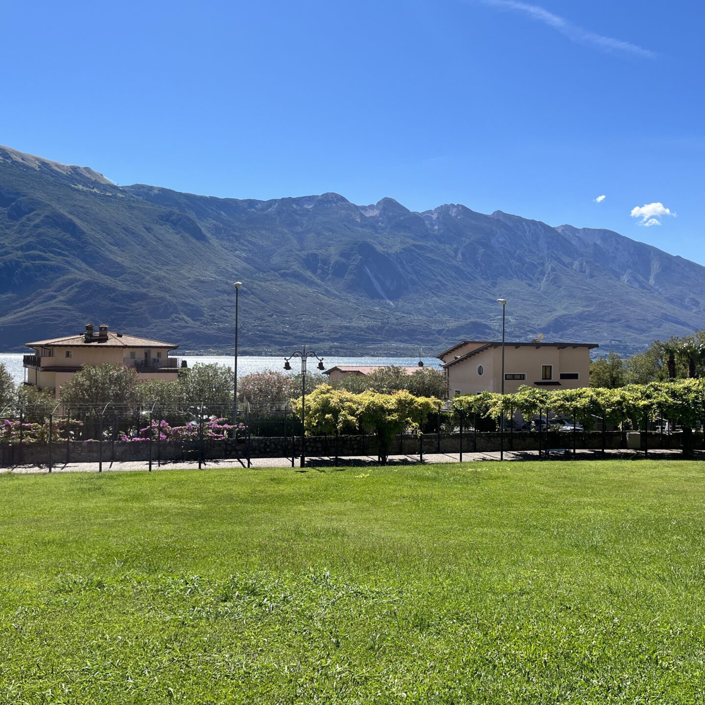 A view of Lake Garda on a sunny day. Large mountains frame the lake in the distance.