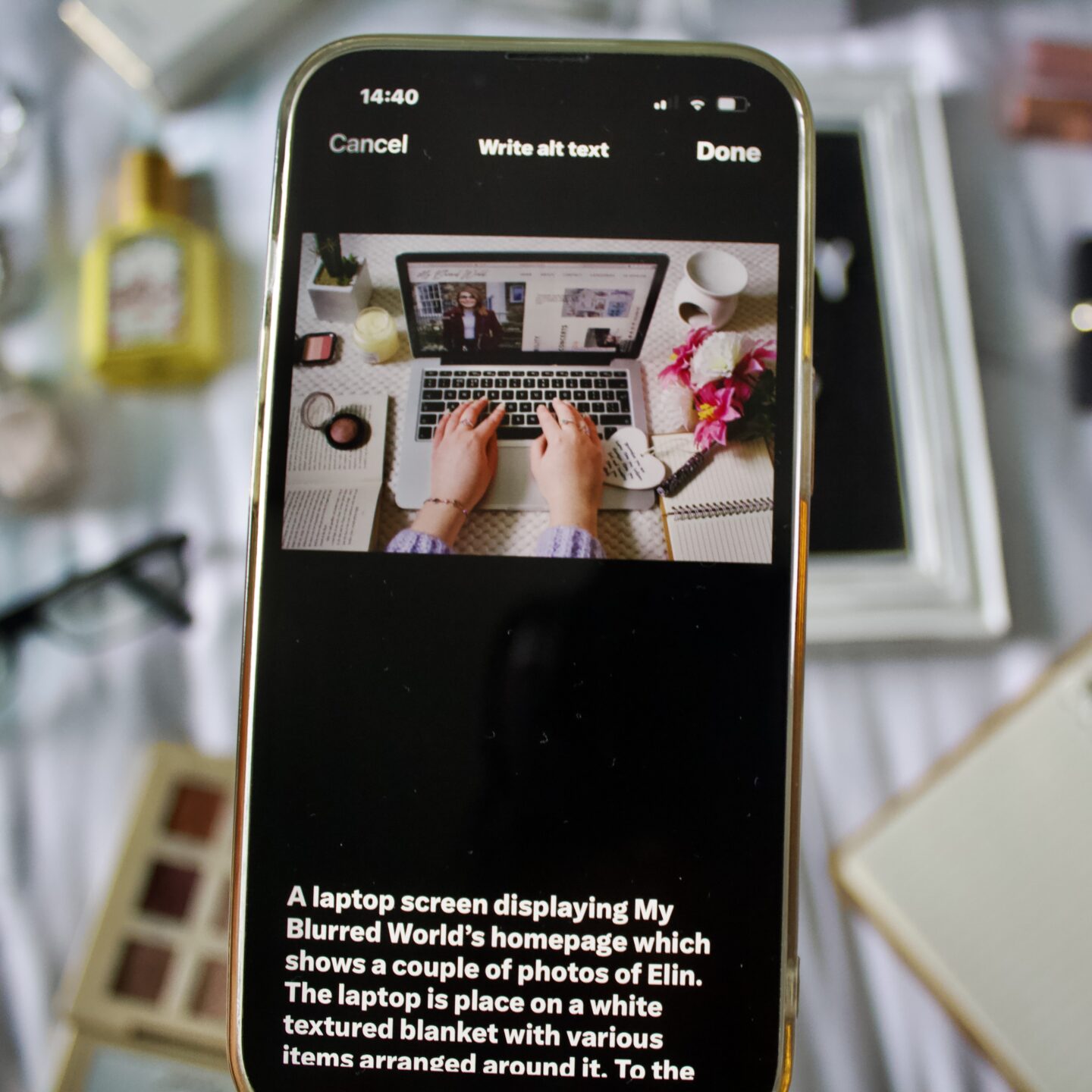 X's Write ALT Text page displayed on a phone screen. It shows a photo at the top with its description below which says 'A laptop screen displaying My Blurred World's homepage which shows a couple of photos of Elin. The laptop is placed on a white textured blanket with various items around it.