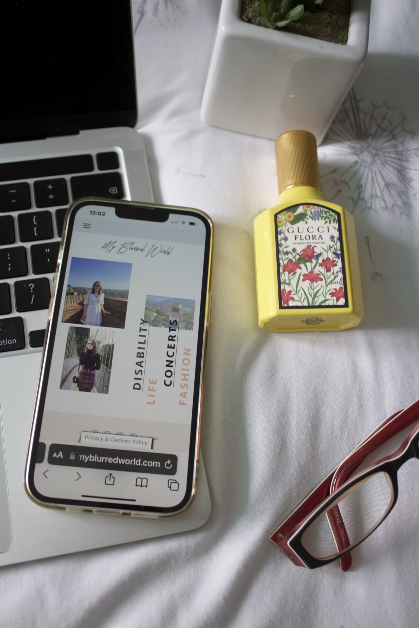 The My Blurred World blog homepage is displayed on a phone screen which rests on the edge of a Macbook keyboard. Beside it is a perfume bottle, a small cactus pot and a pair of glasses.