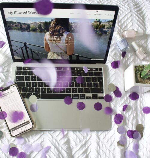 Purple and silver confetti rain down and surround a laptop displaying the My Blurred World blog homepage. A phone is placed on the edge of the laptop keyboard, displaying Elin's first ever blog post titled Introducing My Blurred World.